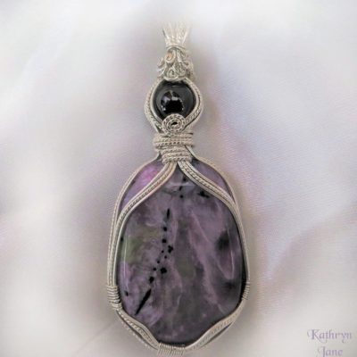 Polished charoite with garnet. Asymmetrical support of sterling silver.