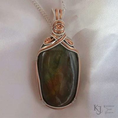 Symmetrical supports of this bronze coloured oval labradorite. Spirals of copper surrounded by sterling silver.
