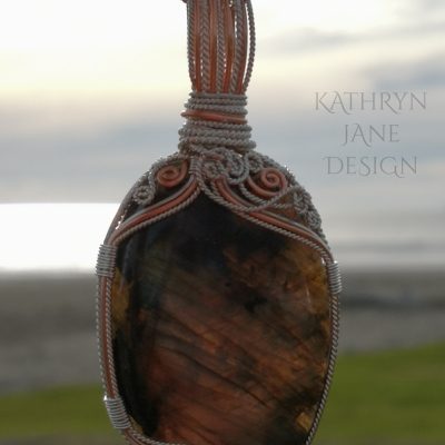 Large oval labradorite pendant, backlit by the setting sun. Asymmetrical supports. Copper and sterling silver spirals.