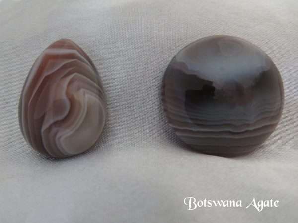 Botswana agate gemstone crystal. Bands of white and brown in a round gemstone and a small teardrop shaped gemstone. White satin background.