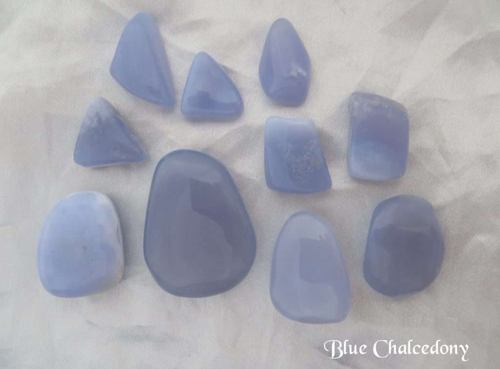 Blue chalcedony polished gemstone crystals in various freeform shapes. Lilac blue in colour, and opaque. White satin background.