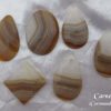 Carnelian, Coromandel, New Zealand Carnelian, gemstone crystals from Coromandel, New Zealand. Bands of white and amber colours in stones shaped like pears, oval and sharp-cornered oblong. White satin background.