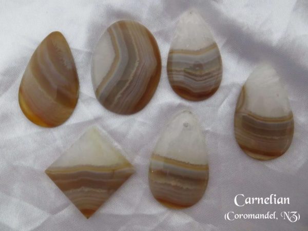Carnelian, Coromandel, New Zealand Carnelian, gemstone crystals from Coromandel, New Zealand. Bands of white and amber colours in stones shaped like pears, oval and sharp-cornered oblong. White satin background.