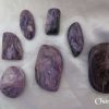 Charoite Charoite gemstone crystals. Purple, black, white and lilac colours swirl through various shaped stones. Oval, oblong, freeform, some cabochons, some tumbled. White satin background.
