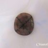 Chiastolite Chiastolite gemstone crystal. Polished stone, slightly round, brown with black cross pattern through entire stone. White satin background.