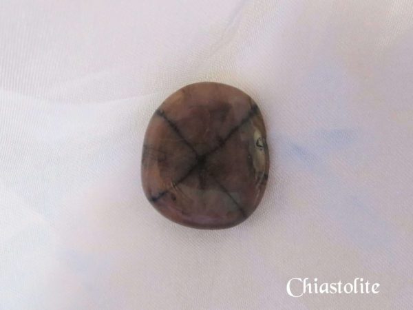 Chiastolite Chiastolite gemstone crystal. Polished stone, slightly round, brown with black cross pattern through entire stone. White satin background.