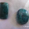 Chrysocolla Chrysocolla gemstone crystals. Opaque, deep turquoise colours. One oblong, and one oval freeform. White satin background.