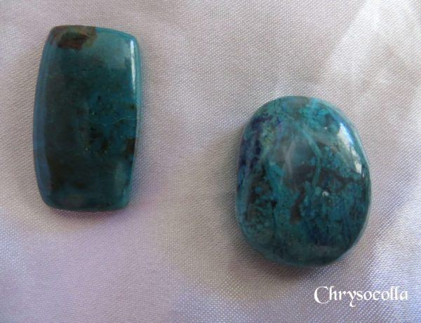 Chrysocolla Chrysocolla gemstone crystals. Opaque, deep turquoise colours. One oblong, and one oval freeform. White satin background.