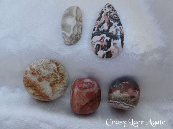 Crazy lace agate Crazy lace agate gemstone crystals. Cabochons and tumbled stones. Multiple patterns and colours within the stones. Freeform oblong, off-white, looks like partially obscured moon peeking out from behind a section of verticle cloud. Bands of grey, white and brown. A pear shaped cabochon, black, white, brown, salmon-pink random patterns. A circle, orange, brown, yellow, off-white. Two tumbled stone, orange-brown patterns.