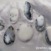 Dendritic agate Dendritic agate gemstone crystal. Seven cabochons, shapes including oval, pear and basically round. White stones with black inclusions, and areas of transparency. White satin background.