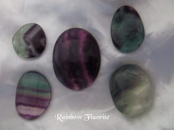 Rainbow fluorite Rainbow fluorite cabochon and polished gemstone crystals. Various shaped gemstones with banded colours of purple, green and transparent on white satin background. All stones have a level of transparency.