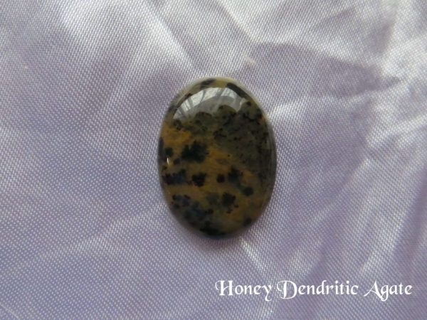 Honey dendritic agate Honey dendritic agate gemstone crystal. Oval cabochon of yellow ochre with black random shapes throughout the stone. White satin background.