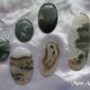 Moss agate Moss agate gemstone crystals. Six oval cabochons, with various degrees of colour and transparency. Greens, white and wee slivers of brown. They look like moss in water. White satin background.