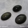 Rainbow obsidian Rainbow obsidian gemstone crystals. Three oval cabochons with rounded tops. Black, opaque, but showing bands of rainbow shimmer near the top. White satin background.