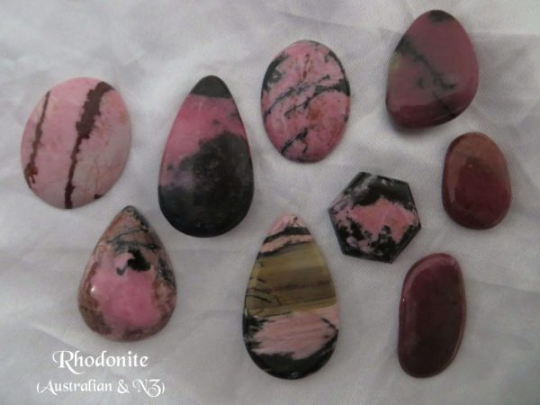 Rhodonite Rhodonite gemstone crystals, from Australia and New Zealand. Nine stones, various shapes and shades of pink with mainly black, some brown, inclusions. Opaque. White satin background.