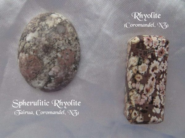 Rhyolite, New Zealand Rhyolite gemstone crystal, New Zealand. Oval and oblong shapes. Bown and peach colours. Oval looks like pebbles under water. Oblong looks like blossoms pressed into a slab of chocolate. White satin background.