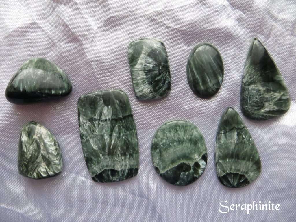Seraphinite gemstone crystals. Six cabochons and two tumbled stones. Shapes include ovals, peardrops and oblongs. Dark green with appearance of pale green wings, hence the association with seraphim angels.