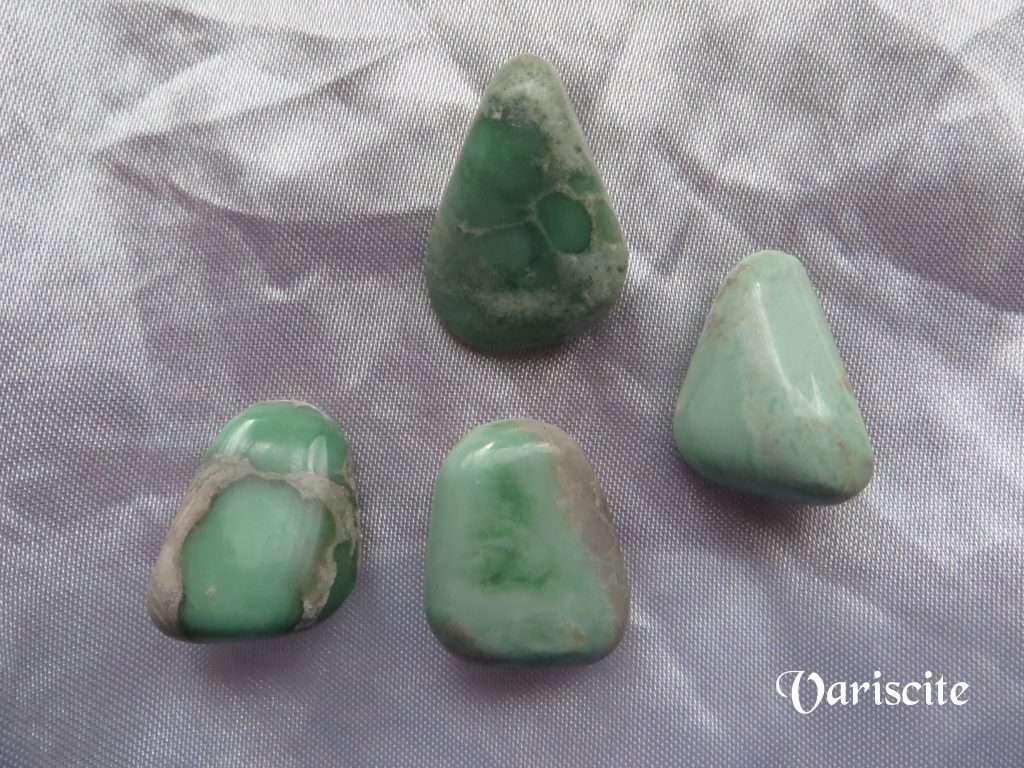 Variscite gemstone crystals, pale green, opaque, tumbled polished stones of various shapes on white satin background.