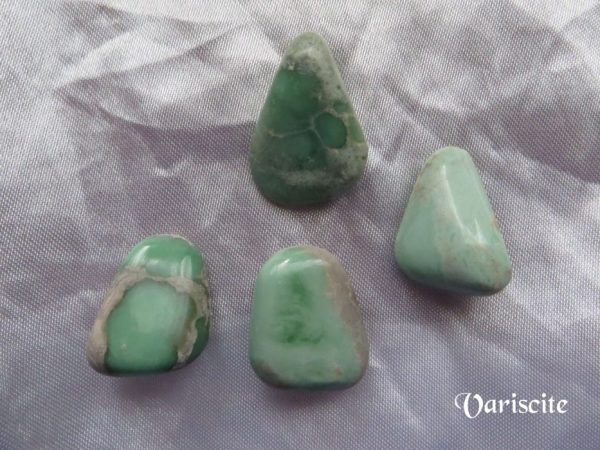 Variscite Variscite gemstone crystals, pale green, opaque, tumbled polished stones of various shapes on white satin background.