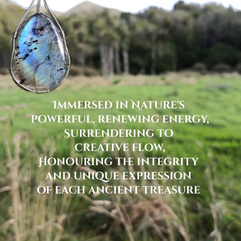 Immersed in Nature's powerful, renewing energy, surrendering to creative flow, honouring the integrity and unique expression of each ancient treasure. A flashing blue labradorite gemstone crystal, wire-wrapped in sterling silver wire, with out of focus grass, trees and hills in the background.