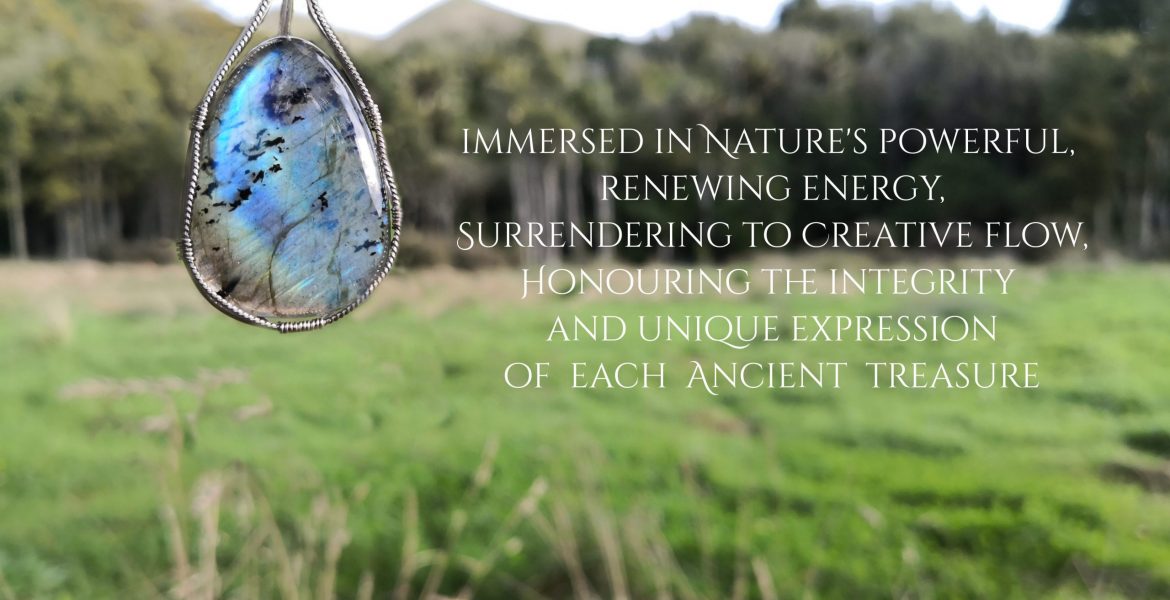 Immersed in Nature's powerful, renewing energy, surrendering to creative flow, honouring the integrity and unique expression of each ancient treasure. A flashing blue labradorite gemstone crystal, wire-wrapped in sterling silver wire, with out of focus grass, trees and hills in the background.