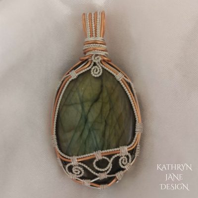 Ornate silverwork with copper frame on oval labradorite
