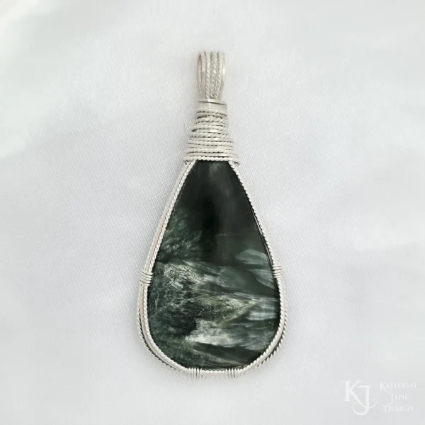 Dark green seraphinite, natural stone, teardrop-shaped pendant, wire-wrapped in twisted sterling silver wire in a simple, outer framework, by Kathryn Jane Design. Plain white background.