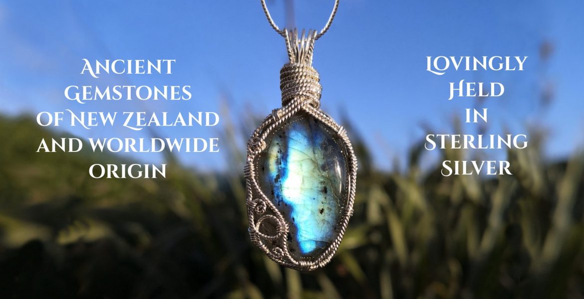Kathryn Jane Design, Ancient gemstones of NZ and worldwide origin, lovingly held in sterling silver. Blue oval labradorite gemstone crystal surrounded by twisted sterling silver wire, with spirals on bottom left. Wires gathered together and folded over at the top, creating a pendant. Background of vivid blue sky, and out of focus green flax.