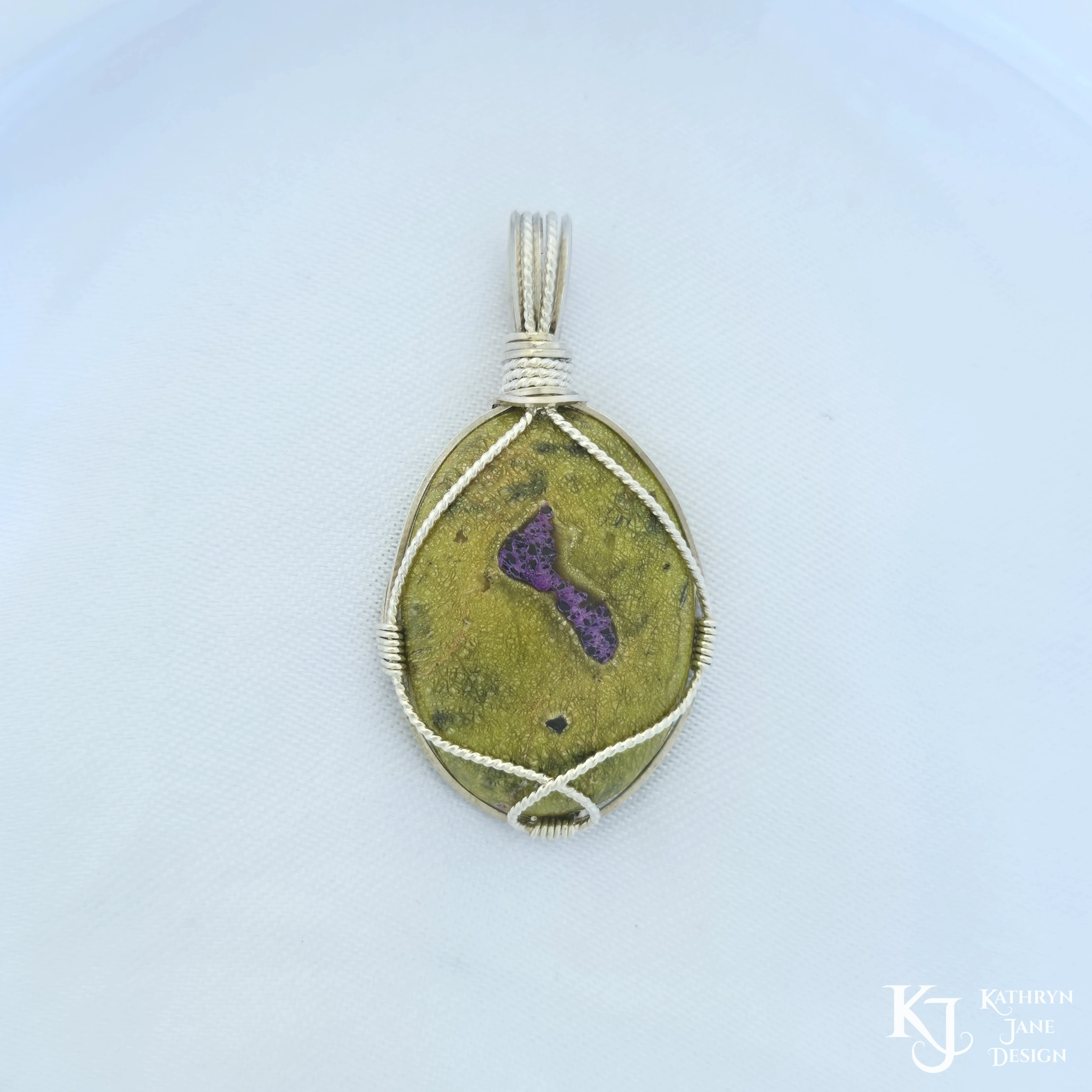Kathryn Jane Design wire-wrapped Atlantisite pendant with sterling silver forming a framework. Purple stichtite in the middle of the green serpentine. White background