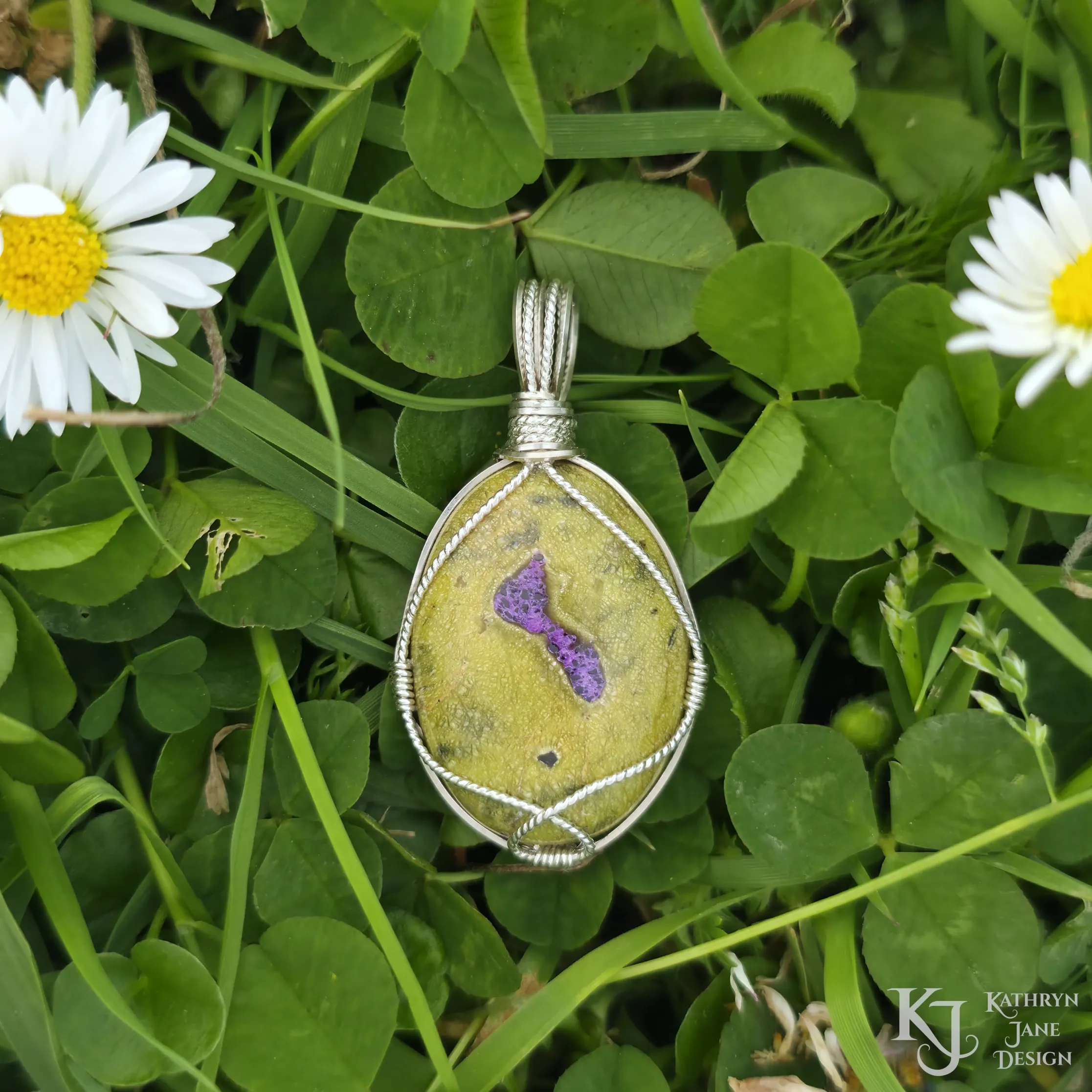 Kathryn Jane Design wire-wrapped Atlantisite pendant with sterling silver forming a framework. Purple stichtite in the middle of the green serpentine. Clover and daisy background