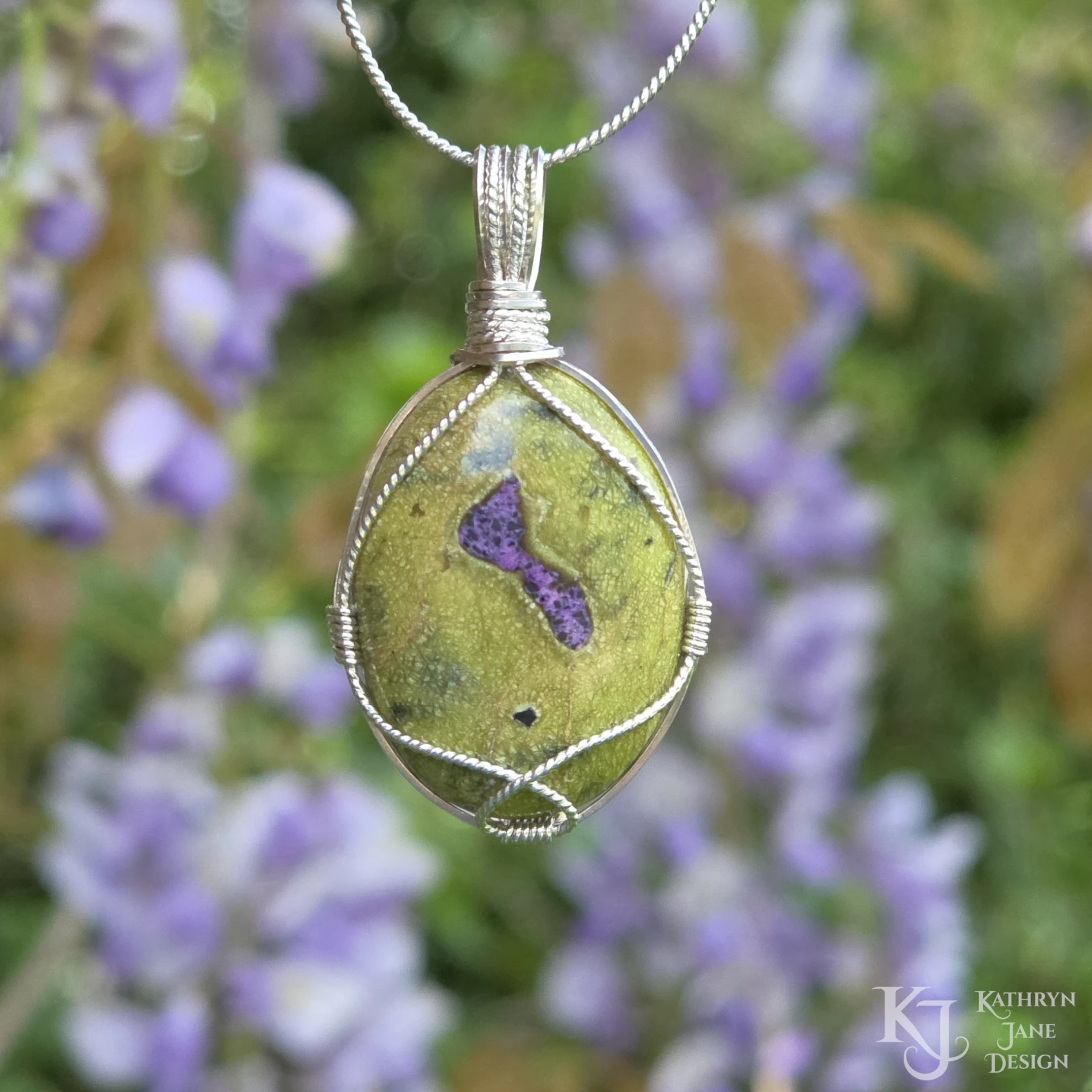 Kathryn Jane Design wire-wrapped Atlantisite pendant with sterling silver forming a framework. Purple stichtite in the middle of the green serpentine. Green and purple background