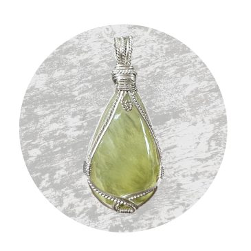 Peardrop-shaped gemstone crystal pendant. Yellow-green in colour, lovingly handcrafted, wire-wrapped in sterling silver. White satin background. Approximate dimensions 45mm long, 20mm wide, 5mm deep. Photograph in natural outdoor light. Old, mossy timber background lightened, so as not to detract from the beauty and calm of the pendant.