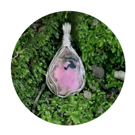 A pink centre to this Kathryn Jane Design rhodonite pendant with swirls of sterling silver forming a framework. Pendant sitting on green moss.