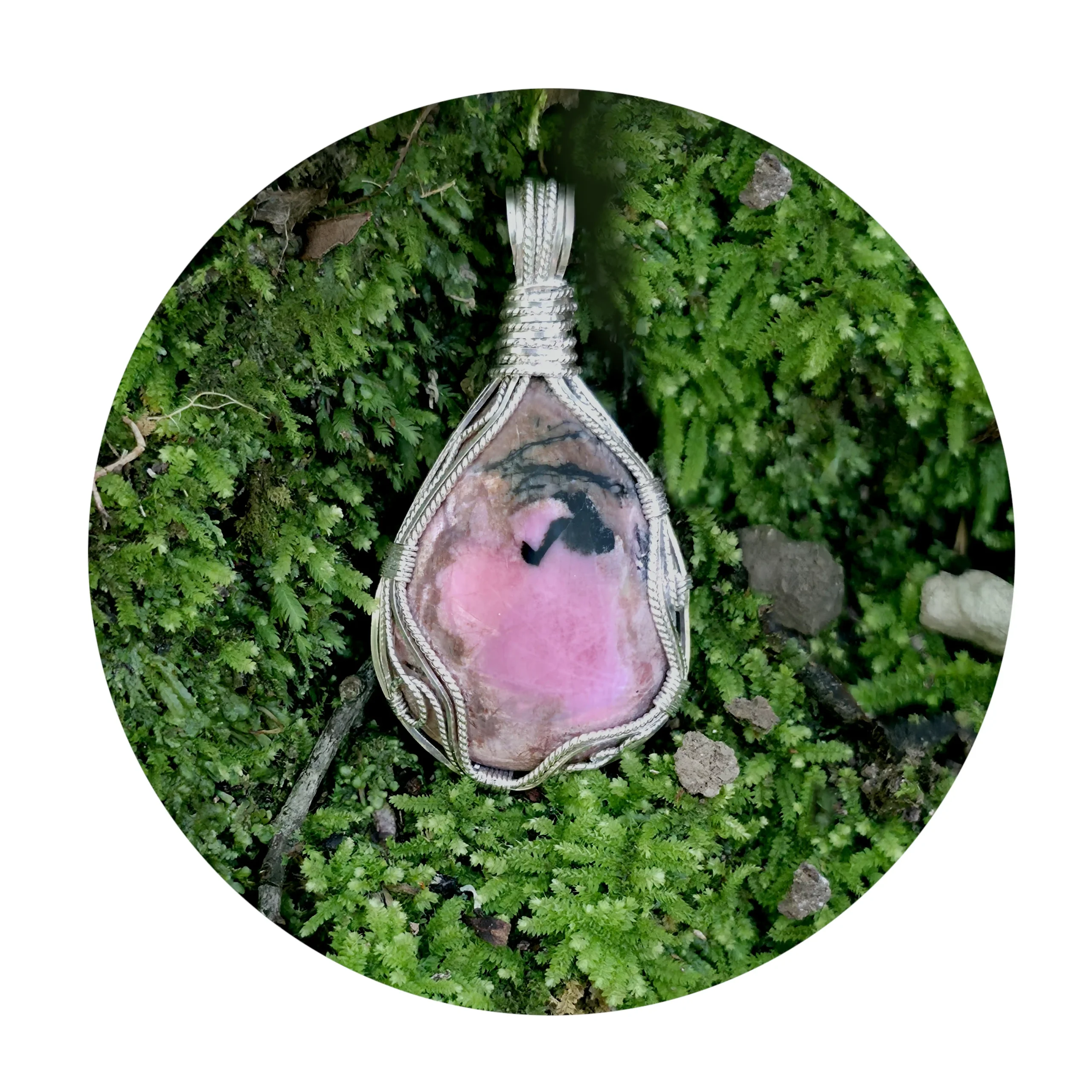 A pink centre to this Kathryn Jane Design rhodonite pendant with swirls of sterling silver forming a framework. Pendant sitting on green moss.