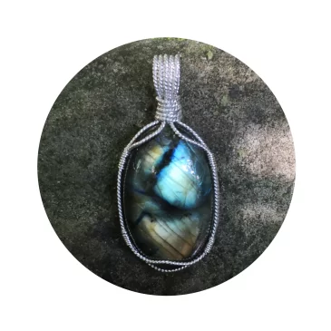 Guardian angel labradorite pendant by Kathryn Jane Design. Oval labradorite gemstone crystal wire-wrapped in twisted sterling silver. Pendant on a natural river stone. Flashes of blue, green and gold with branch-looking patterns of black across the face of the pendant