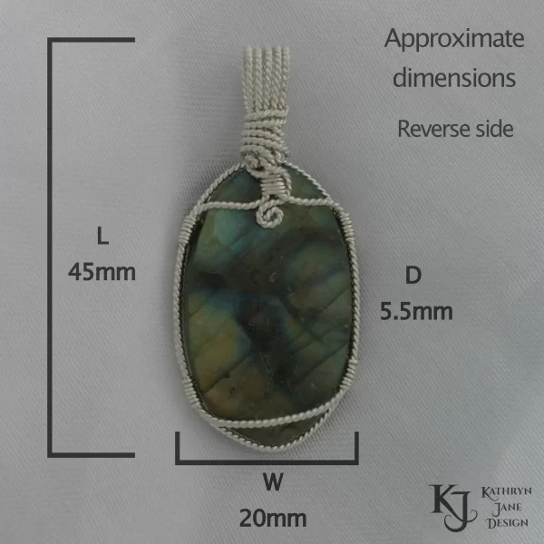 Labradorite gemstone crystal, wire-wrapped in twisted sterling silver, on white satin background. Reverse side of stone. Approximate dimensions, 45mm log, 20mm wide, and 5.5mm deep. Flashes of blue, green, gold with black branch-like lines running across the face.