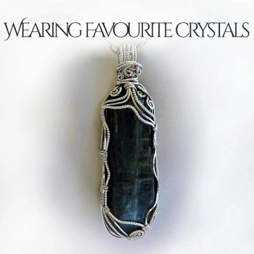 Wearing favourite crystals. Favourite stones get transformed into pendants. Large dark blue kyanite gemstone crystal wire-wrapped in sterling silver, with spirals at the top of the pendant. White satin background.
