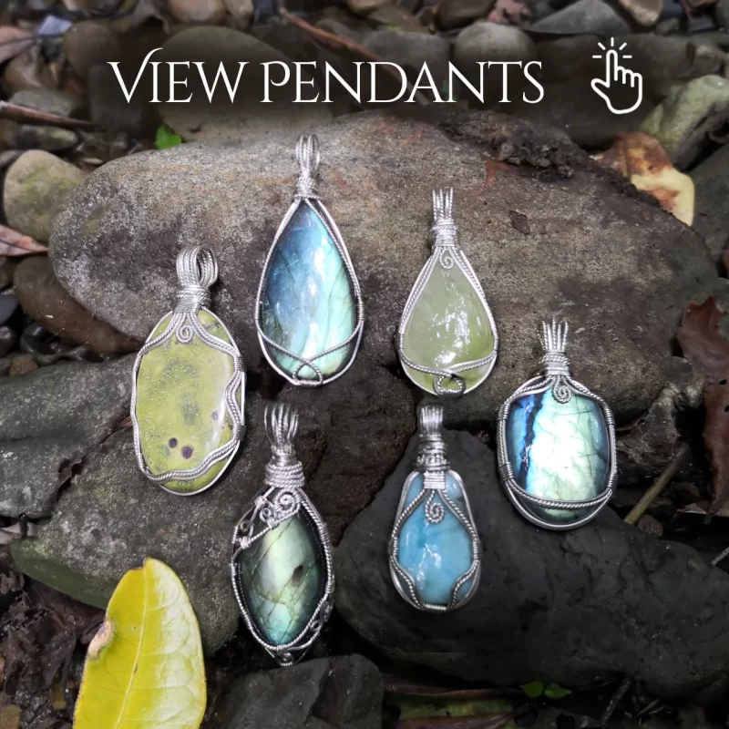 View available Kathryn Jane Design gemstone pendants. Natural gemstone crystal pendants, wire-wrapped in sterling silver, on stones of riverbed, surrounded by leaves. Crystals include Atlantisite (stichtite in serpentine), labradorite, prehnite and larimar.