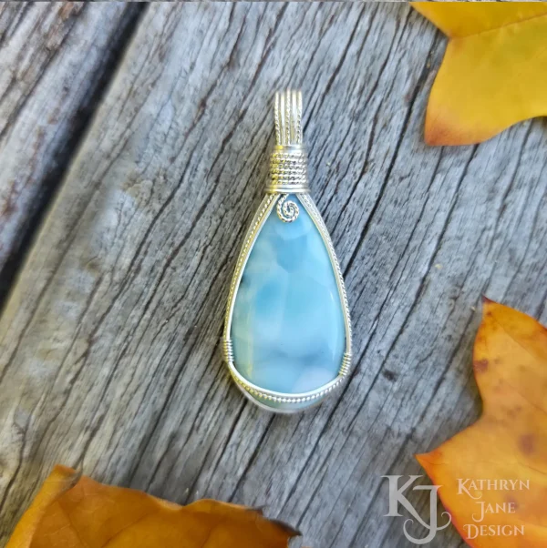 Peardrop-shaped larimar pendant, soft blue-turqoise, framed in sterling silver wire. Kathryn Jane Design wire wrapped pendant. Edges of three golden-coloured autumn leaves