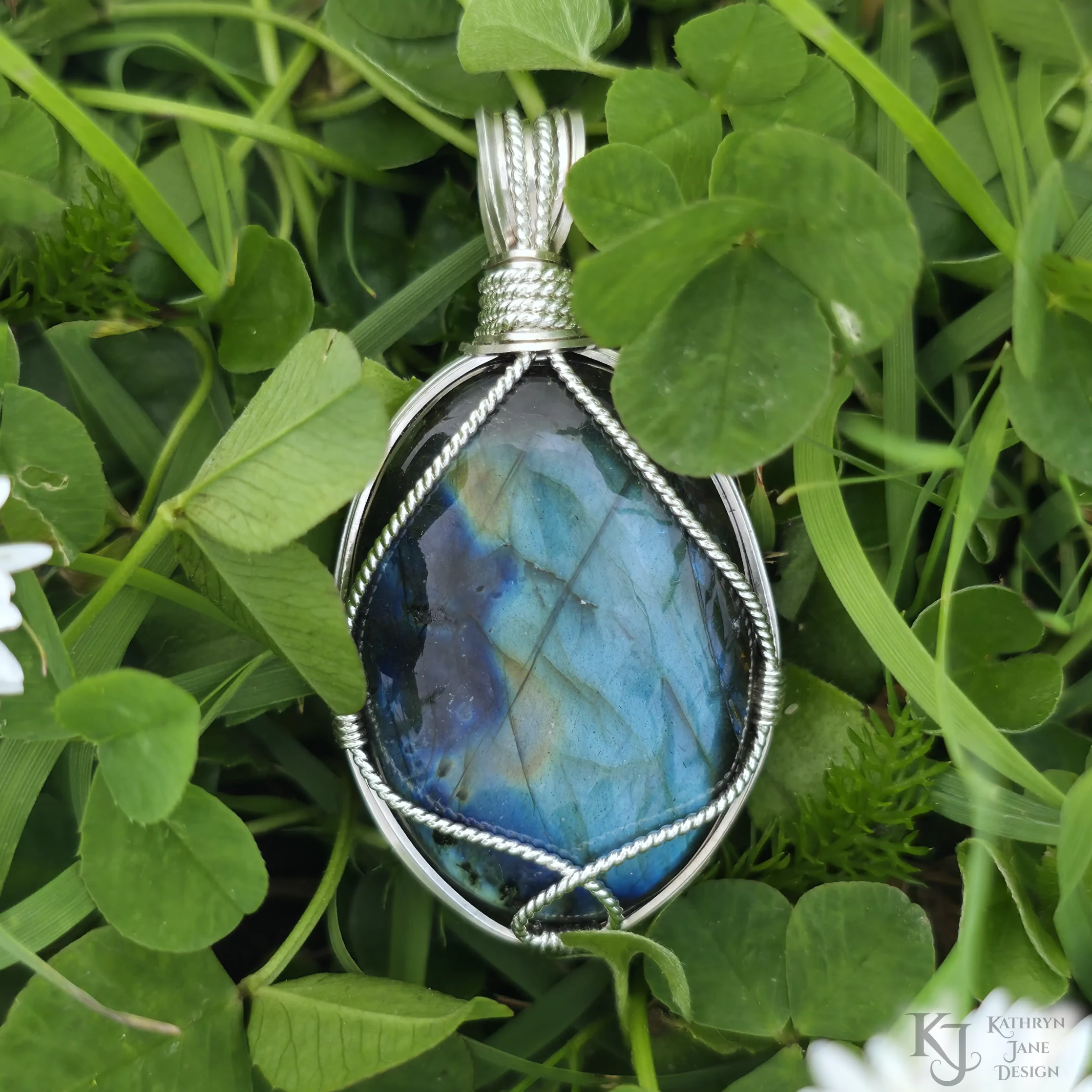 Kathryn Jane Design wire-wrapped labradorite pendant with sterling silver forming a framework. Grass background.