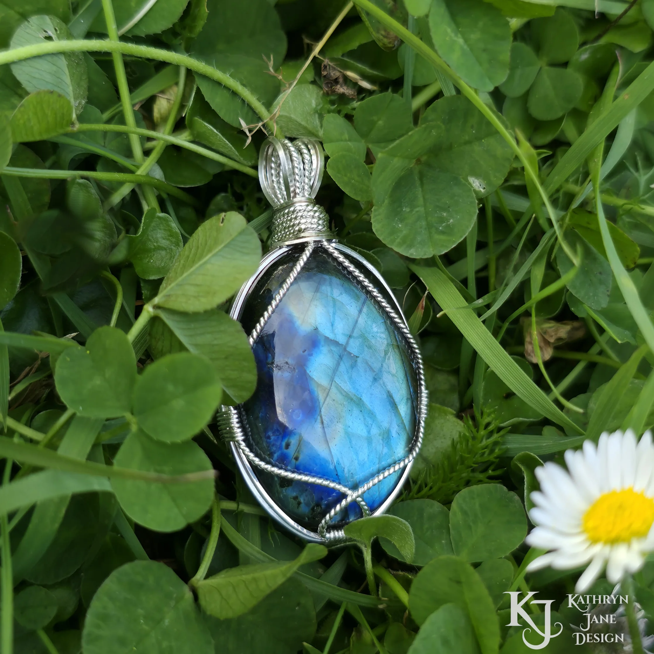 Kathryn Jane Design wire-wrapped labradorite pendant with sterling silver forming a framework. Grass background.