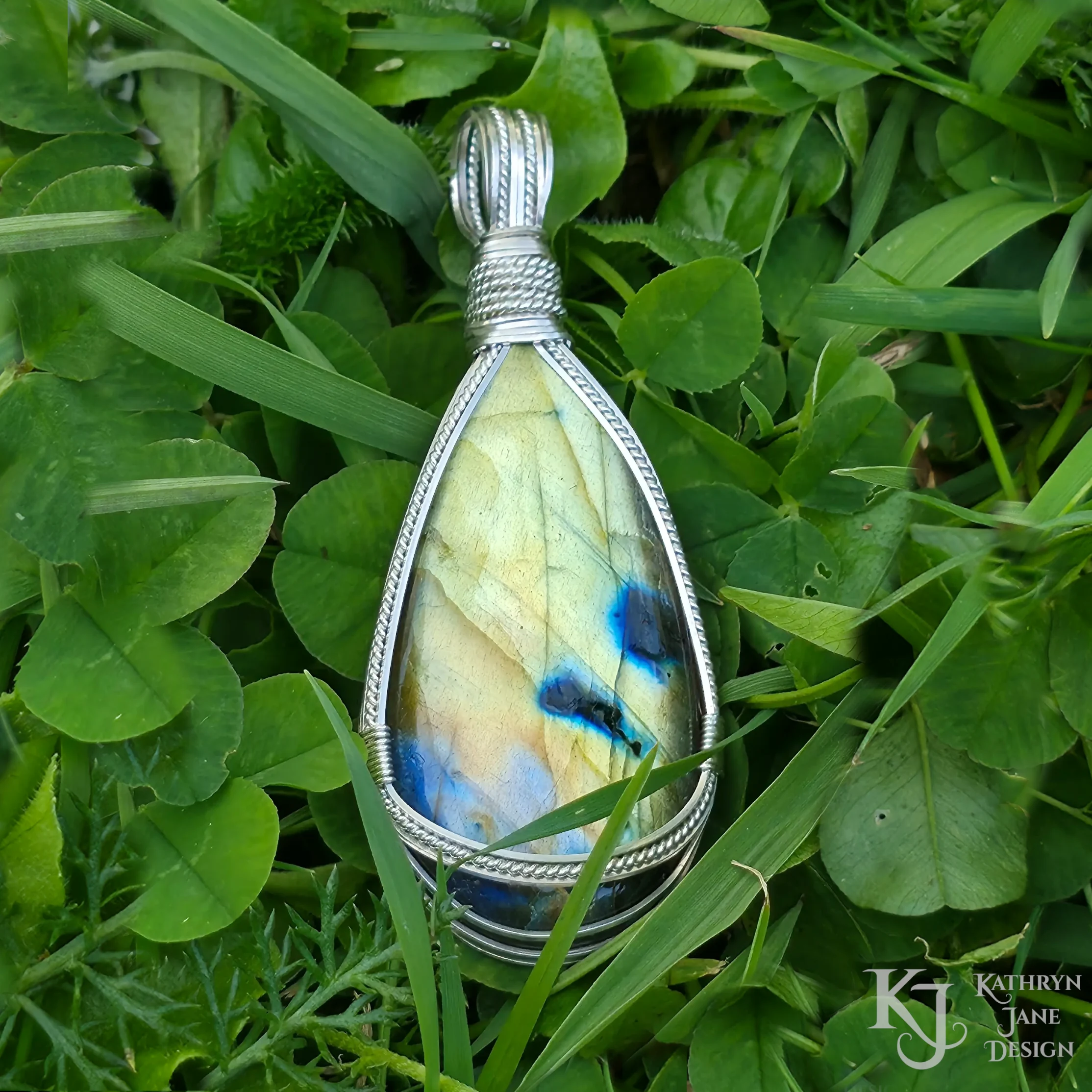 Kathryn Jane Design wire-wrapped labradorite pendant with sterling silver forming a framework. Grass background.