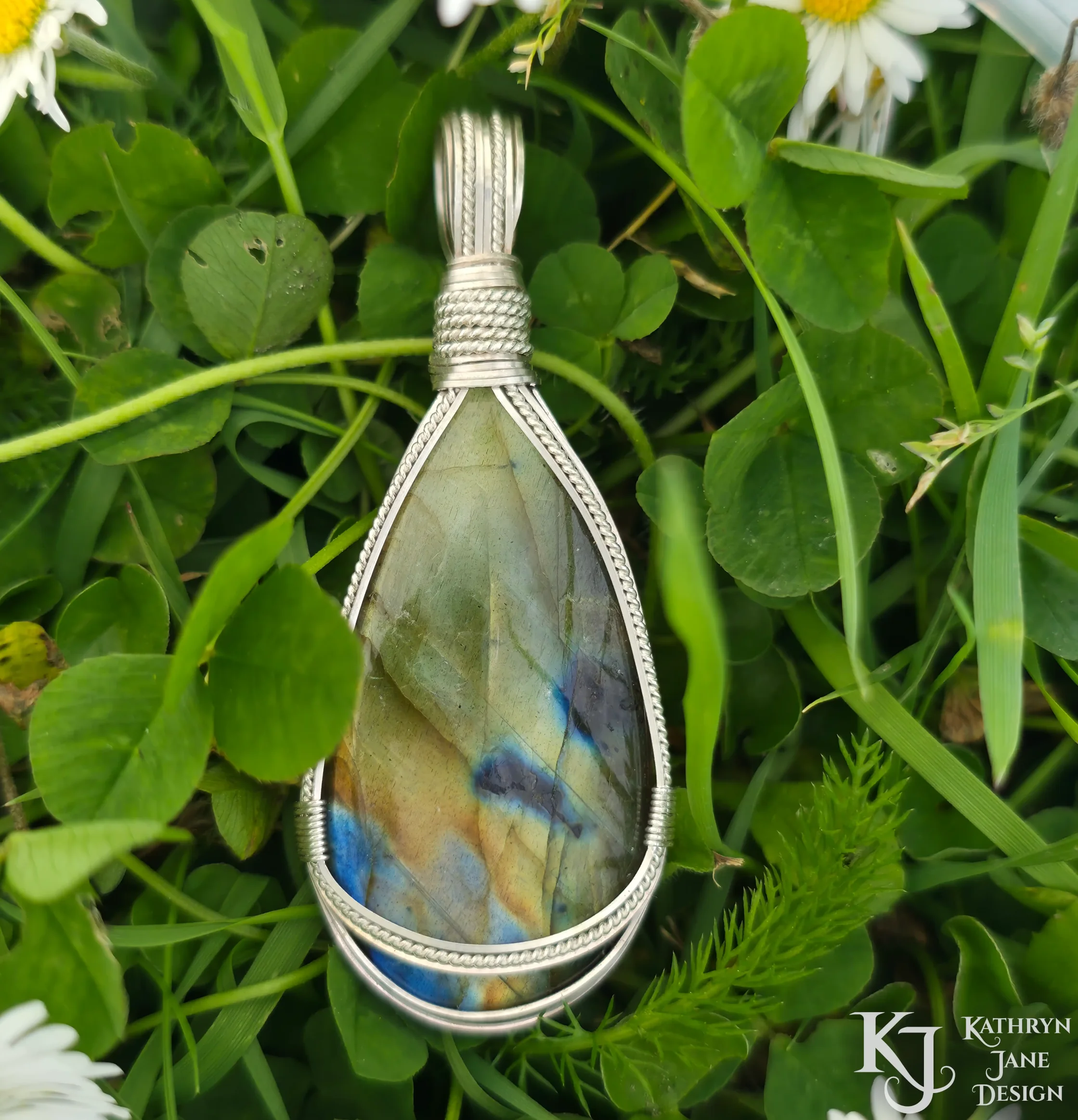 Kathryn Jane Design wire-wrapped labradorite pendant with sterling silver forming a framework. Grass background.