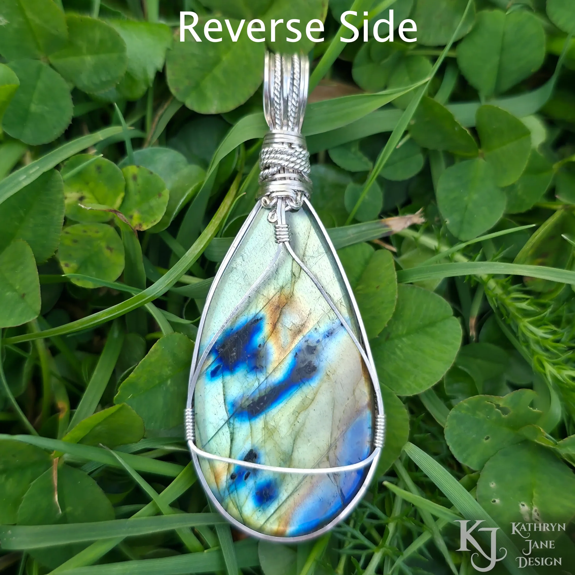 Kathryn Jane Design wire-wrapped labradorite pendant with sterling silver forming a framework. Grass background.