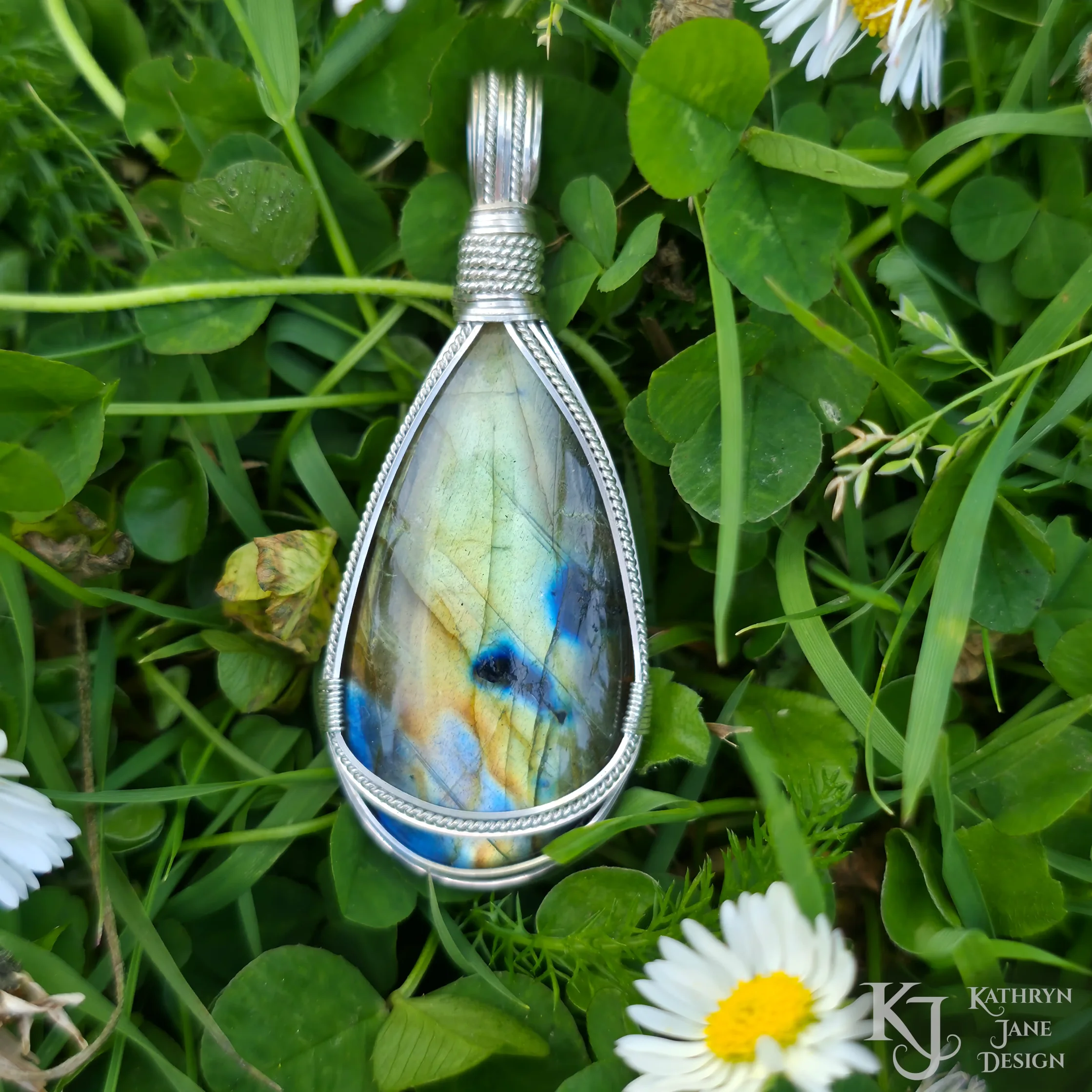 Kathryn Jane Design wire-wrapped labradorite pendant with sterling silver forming a framework. Grass background.
