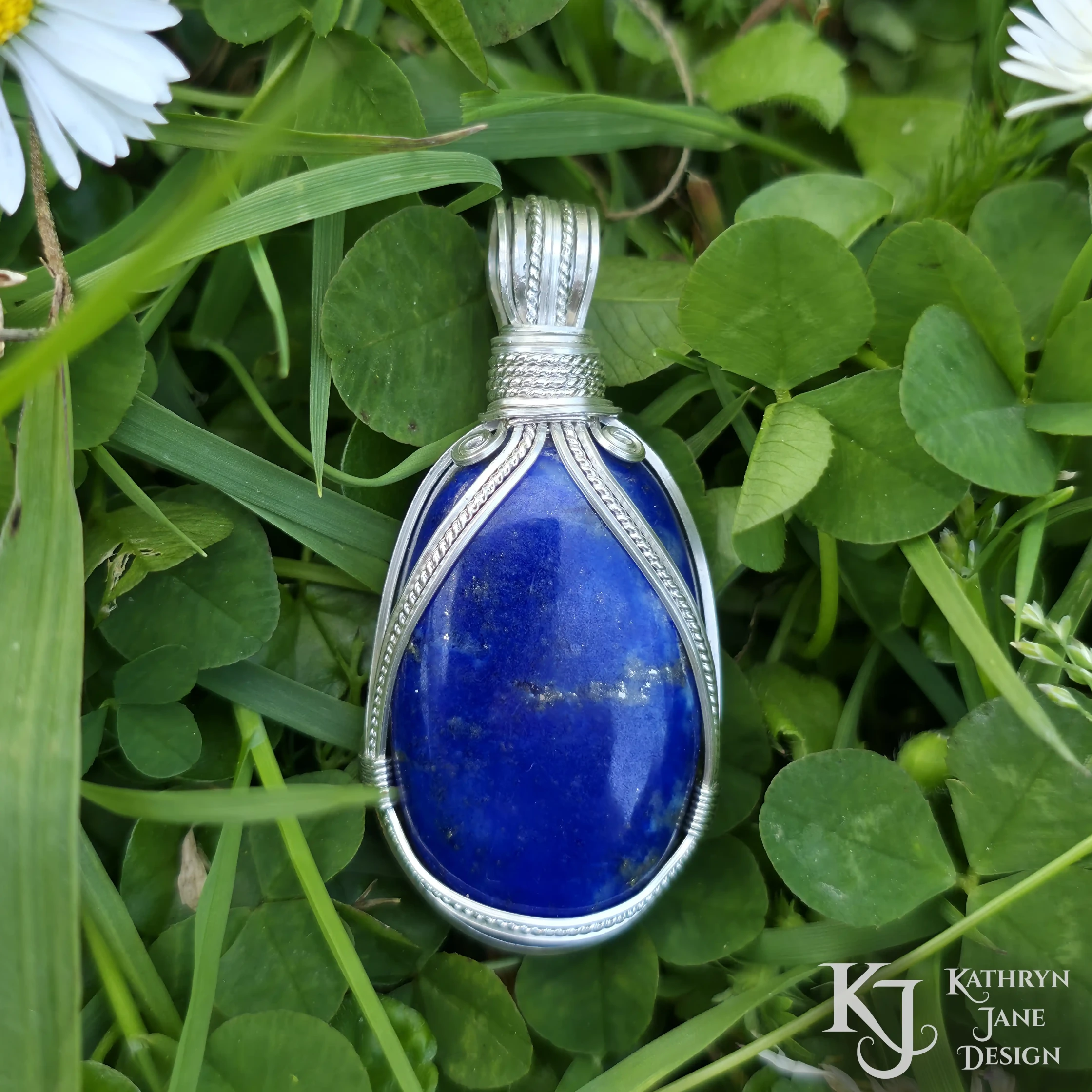 Kathryn Jane Design wire-wrapped lapis lazuli pendant with sterling silver forming a framework. Grass background.