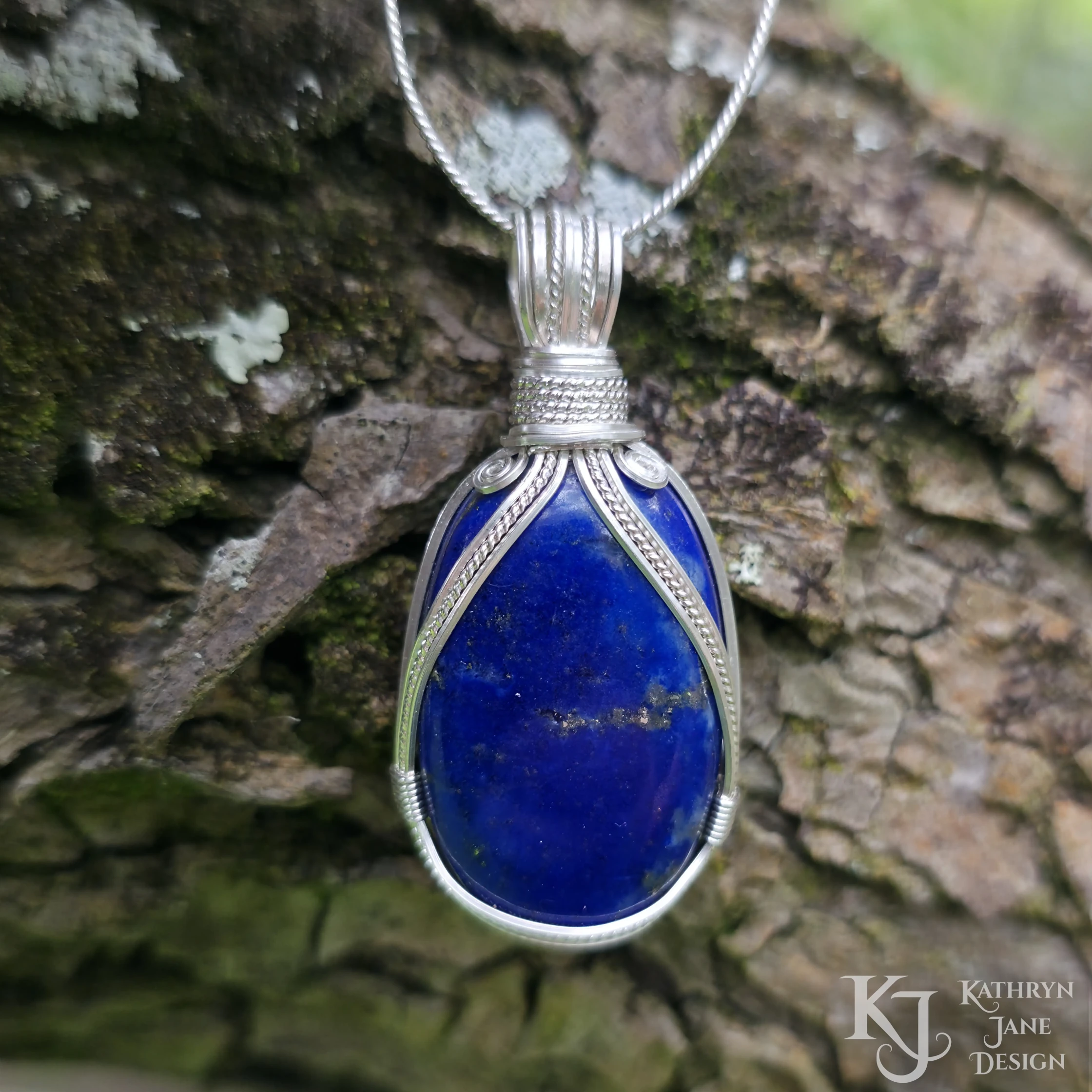Kathryn Jane Design wire-wrapped lapis lazuli pendant with sterling silver forming a framework. Bark background.