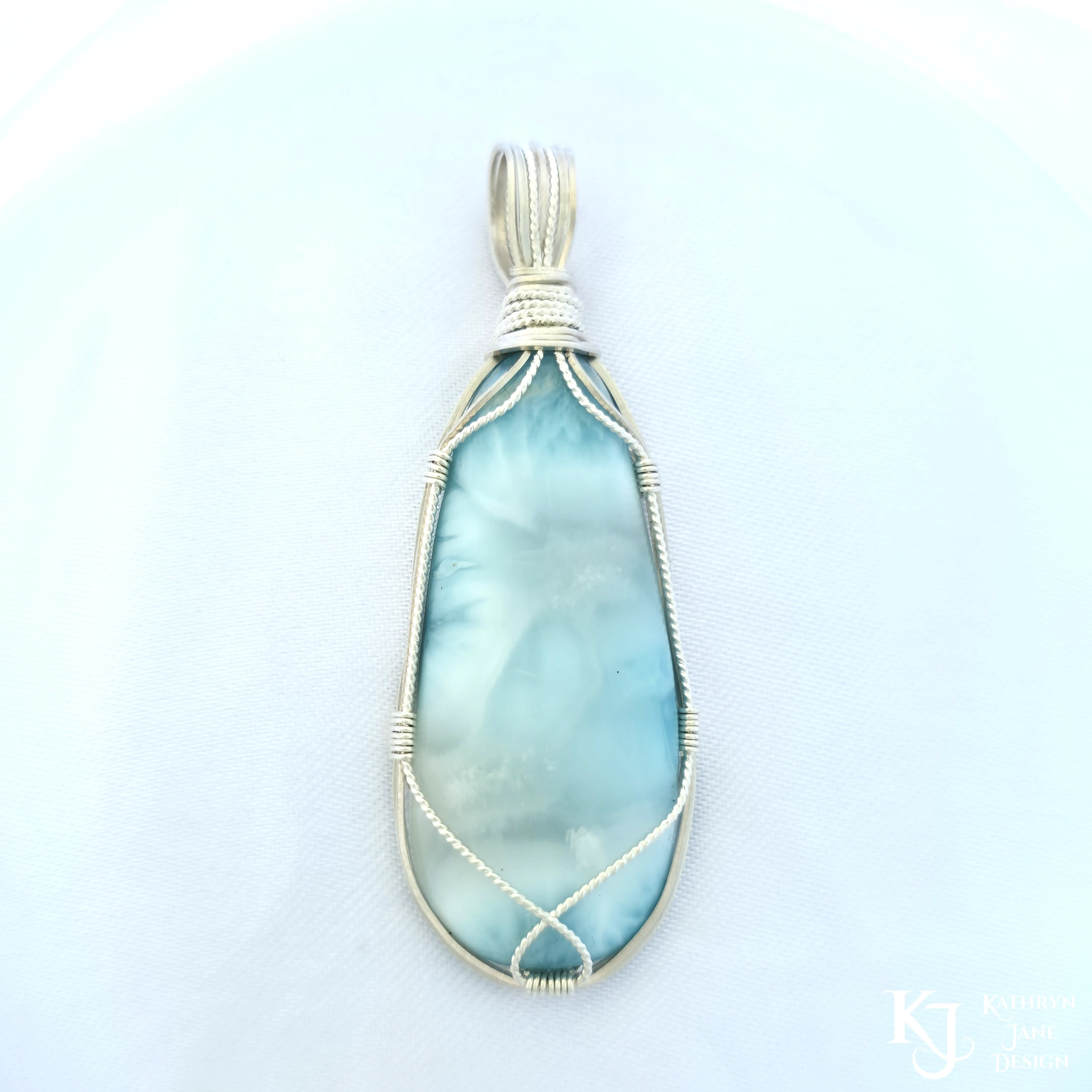 Turquoise-blue larimar pendant, with square and twisted sterling silver wire support and bail by Kathryn Jane Design. Plain white background