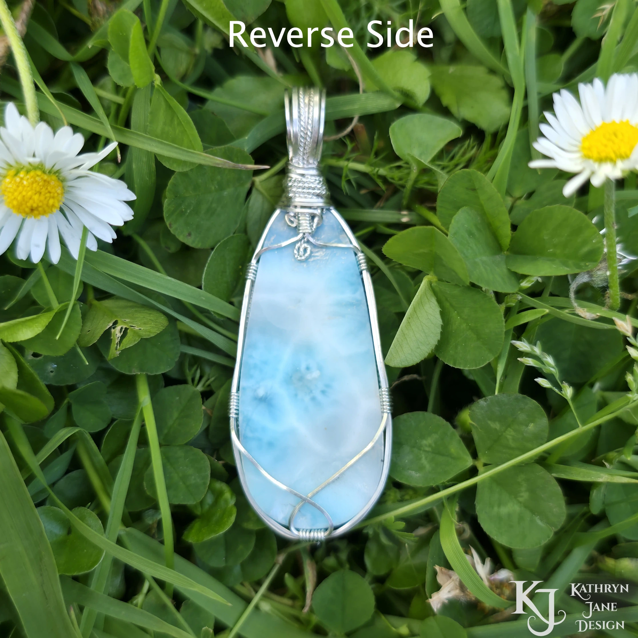 Reverse side of turquoise-blue larimar pendant, with square and twisted sterling silver wire support and bail by Kathryn Jane Design. Green clover background with two white daisies with yellow centres.