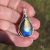 In direct, bright sunlight Triangular-shaped natural labradorite pendant in a simple sterling silver framework in hand in bright sunlight. Labradorescence showing brilliant gold and electric blue